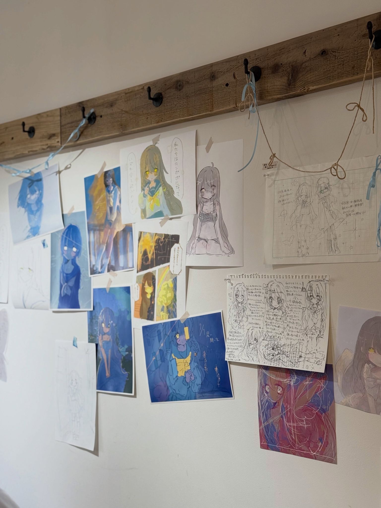 2階の白い壁に、額入りの絵や紙の作品が並べて展示されている